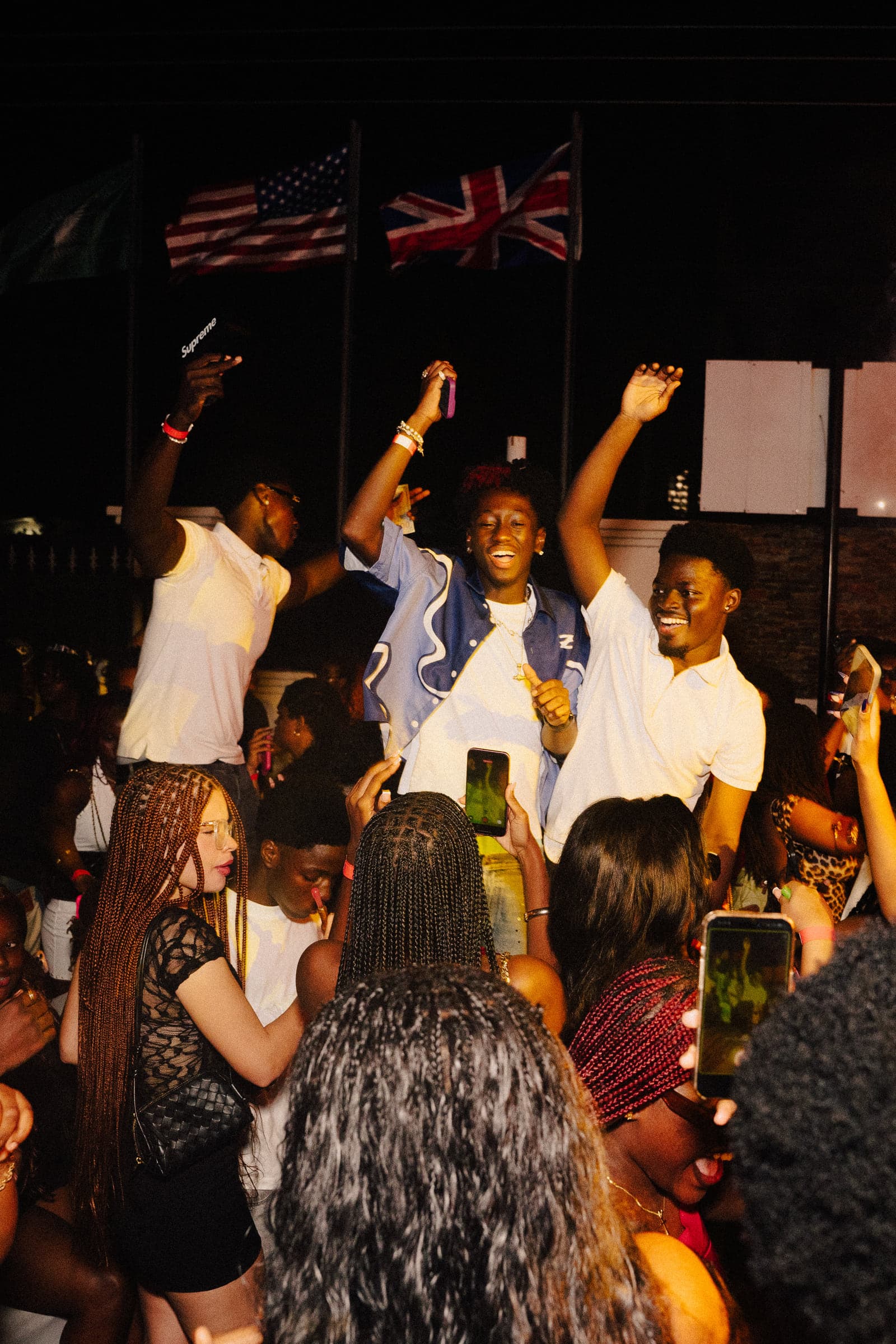Guests going wild on stage, drinks and phones in the air under the flags