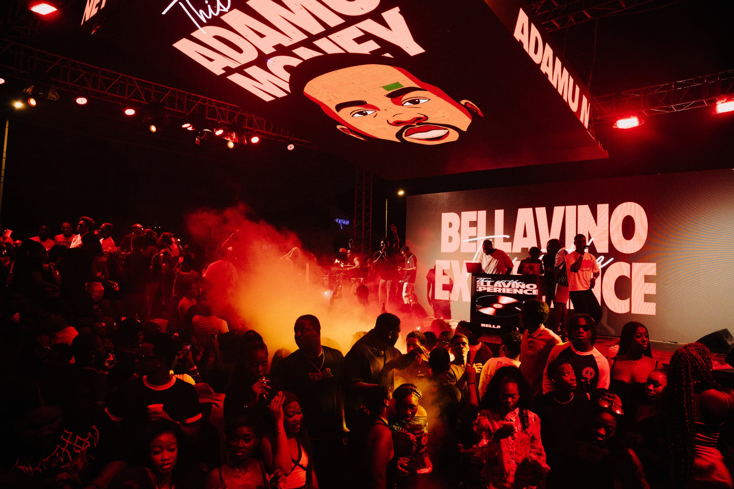 Smoke cannons fire over a packed crowd while the BELLAVINO EXPERIENCE screen glows behind the stage